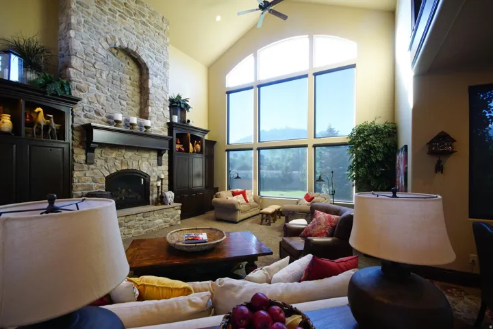 Great room featuring a floor-to-ceiling stone fireplace with an arched hearth, custom built-in cabinetry, and a vaulted ceiling
