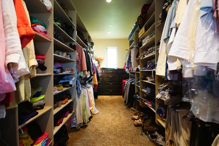 Spacious walk-in closet featuring extensive built-in shelving, multiple hanging rods, dark wood-finish cabinetry, and a window providing natural light