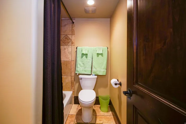 Bathroom featuring a white toilet, ceramic tile flooring, ceramic tile shower surround, and a dark wood panel door