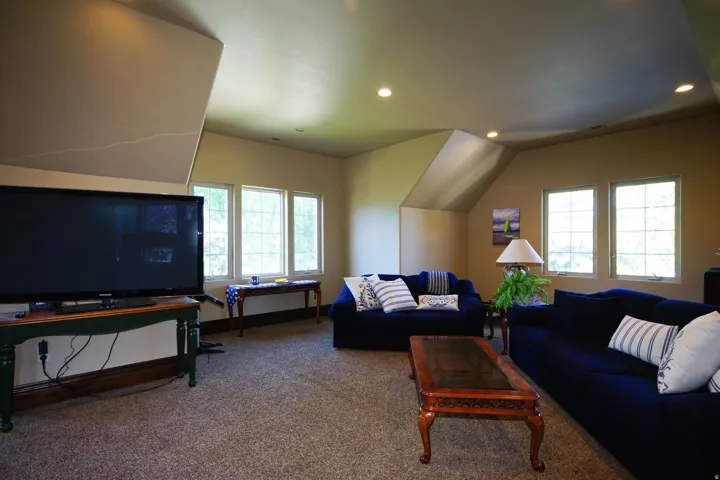 Spacious room featuring carpeting, multiple windows providing natural light, recessed ceiling lights, and sloped ceiling details