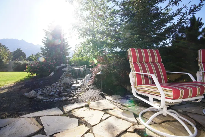 Flagstone patio featuring a rock-lined water feature, mature trees, and a manicured lawn