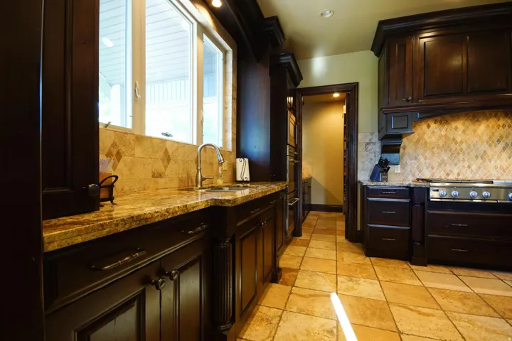 Kitchen featuring dark wood-finish cabinetry, light-toned tiled flooring, a tiled backsplash with diamond accents, and a stainless steel sink with a gooseneck faucet