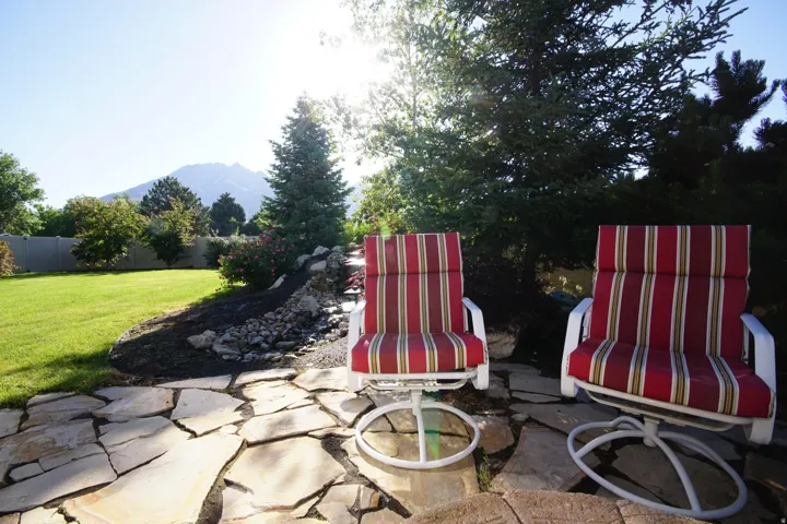 Expansive backyard featuring flagstone patio, manicured lawn, established landscaping, mature evergreen trees, and mountain scenery