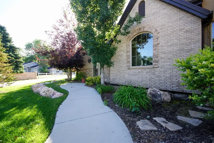 Brick exterior with an arched window, a curved concrete pathway, mature trees, landscaped shrubbery, and decorative rocks
