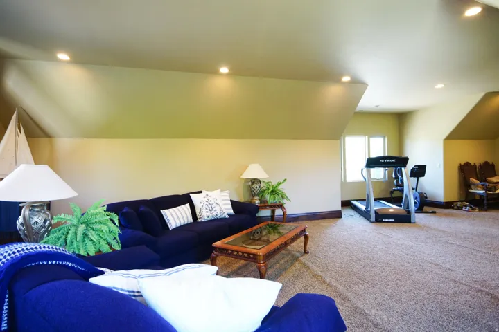 Expansive room with sloped ceilings, recessed lighting, carpet flooring, a multi-pane window, and substantial baseboards