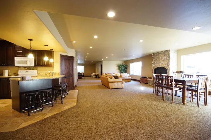 Expansive open-concept living area featuring a full-size kitchen with dark wood cabinetry and stone countertops, a stone fireplace, recessed lighting, and multiple windows