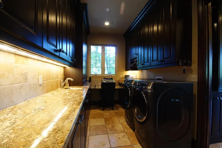 Dedicated utility room featuring dark wood cabinetry, a light-toned patterned stone countertop with an undermount sink, and tiled flooring