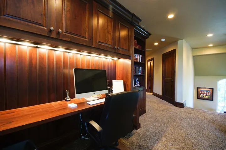 Dedicated office space featuring rich wood-finish built-in cabinetry, under-cabinet lighting, and a wood-finish desk surface