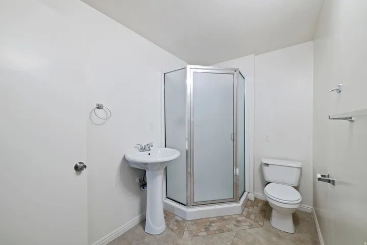Bathroom featuring a corner shower with frosted glass enclosure, pedestal sink, and toilet