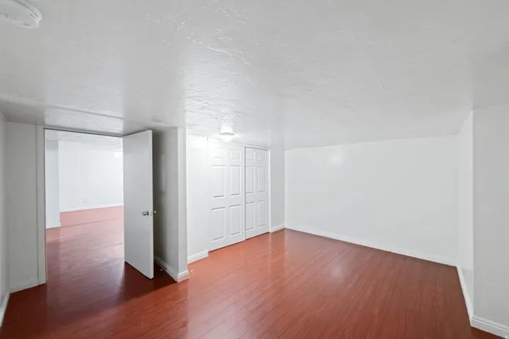 Spacious room featuring wood-finish flooring, white painted walls, and a ceiling-mounted light fixture