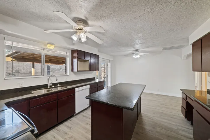 Kitchen featuring a central island, dark wood-finish cabinetry, granite-style countertops, stainless steel sink, and wood-finish flooring