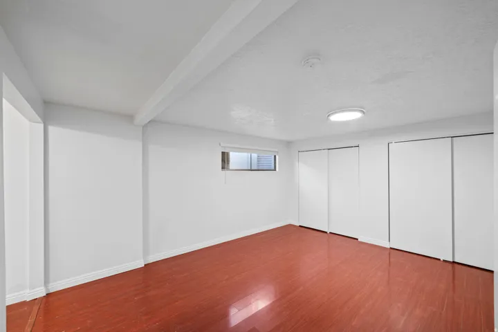Spacious room featuring wood-finish flooring, white walls, and a ceiling-mounted light fixture