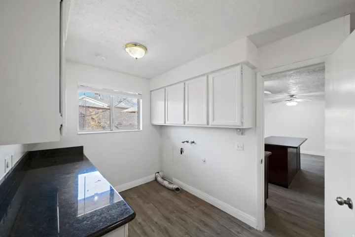 Laundry area featuring a dark stone-finish countertop, white cabinetry, a window, and wood-finish flooring