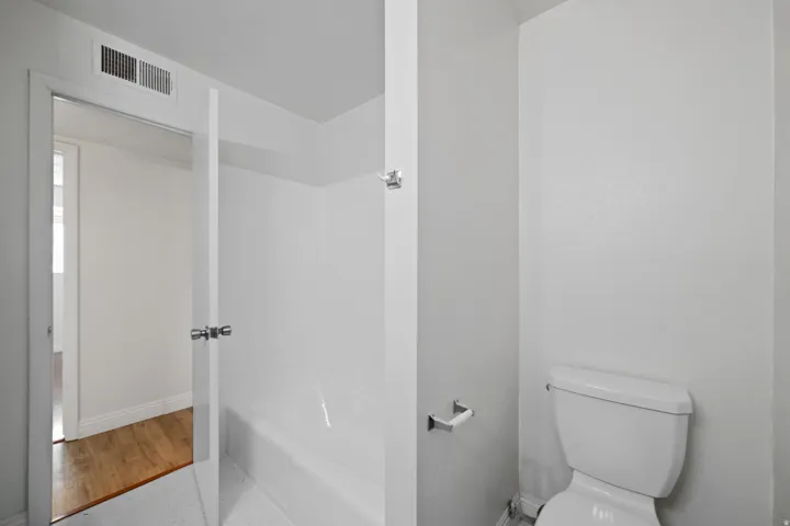 Bathroom featuring a white tub/shower combination, white toilet, and light gray walls