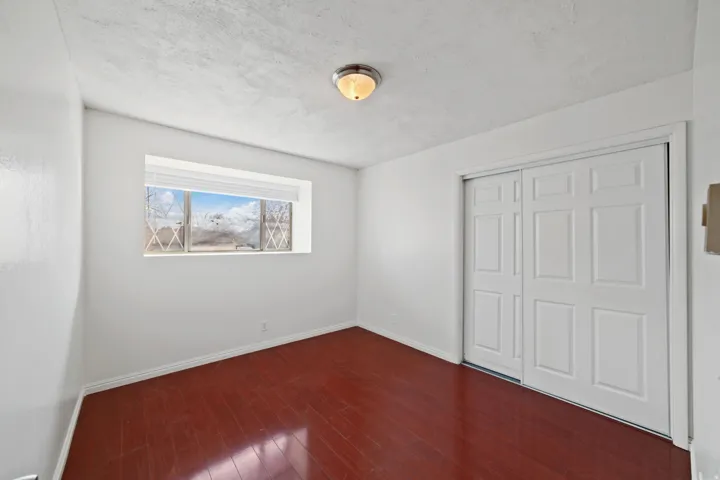 Interior room featuring rich wood-finish flooring, white walls, and a window with blinds