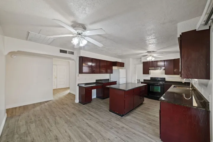 Open-concept living space featuring wood-finish flooring, dark wood cabinetry, a central kitchen island, and multiple ceiling fans