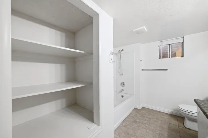 Bathroom featuring a white bathtub with shower, toilet, and a window with blinds
