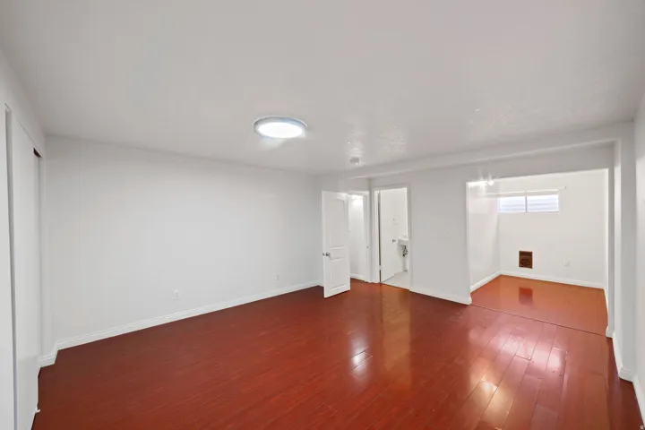 Spacious room featuring rich wood-finish flooring, crisp white walls, and a recessed ceiling light fixture