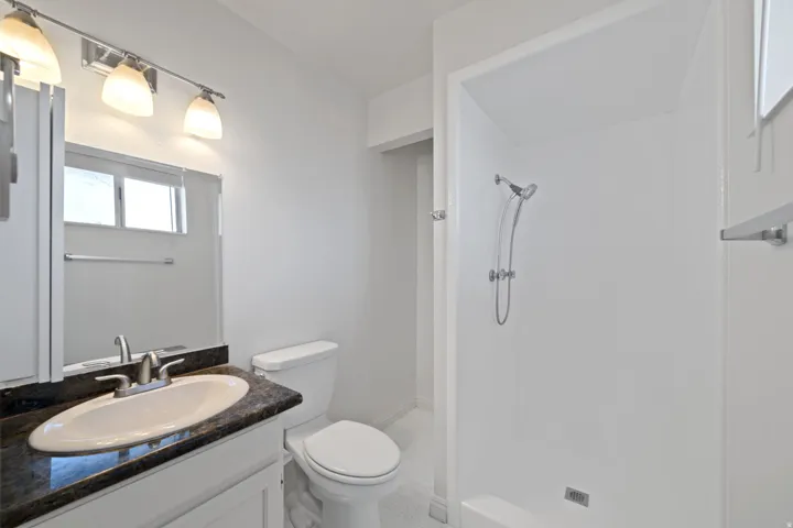 Bathroom featuring a single vanity with a dark stone countertop and oval undermount sink, a chrome faucet, and overhead lighting