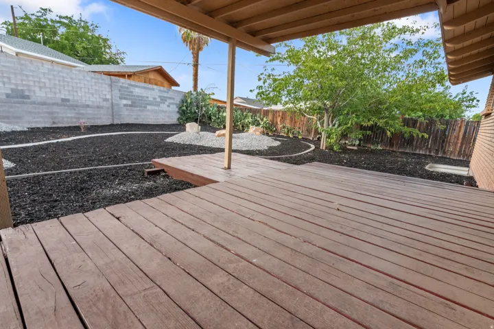 Expansive wooden deck with a covered patio area, overlooking a backyard featuring a perimeter block wall, a secondary wooden fence, and landscaping with dark mulch and decorative rocks