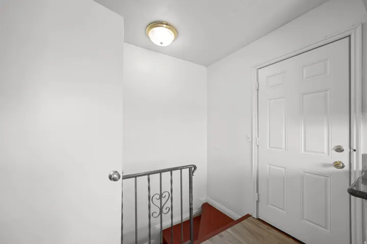 Entryway featuring a paneled door with polished brass hardware, a gold-finish ceiling light fixture, and a decorative wrought iron railing