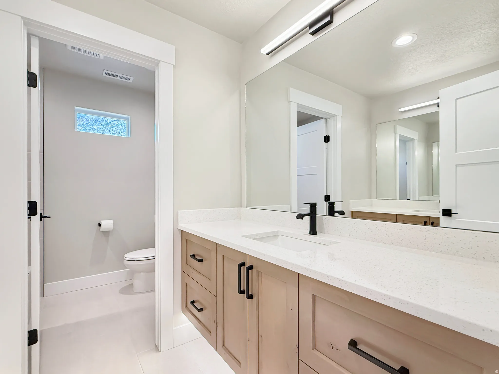 Bathroom vanity featuring light wood-finish cabinetry with matte black hardware, a light-colored speckled countertop, and an undermount sink with a black faucet