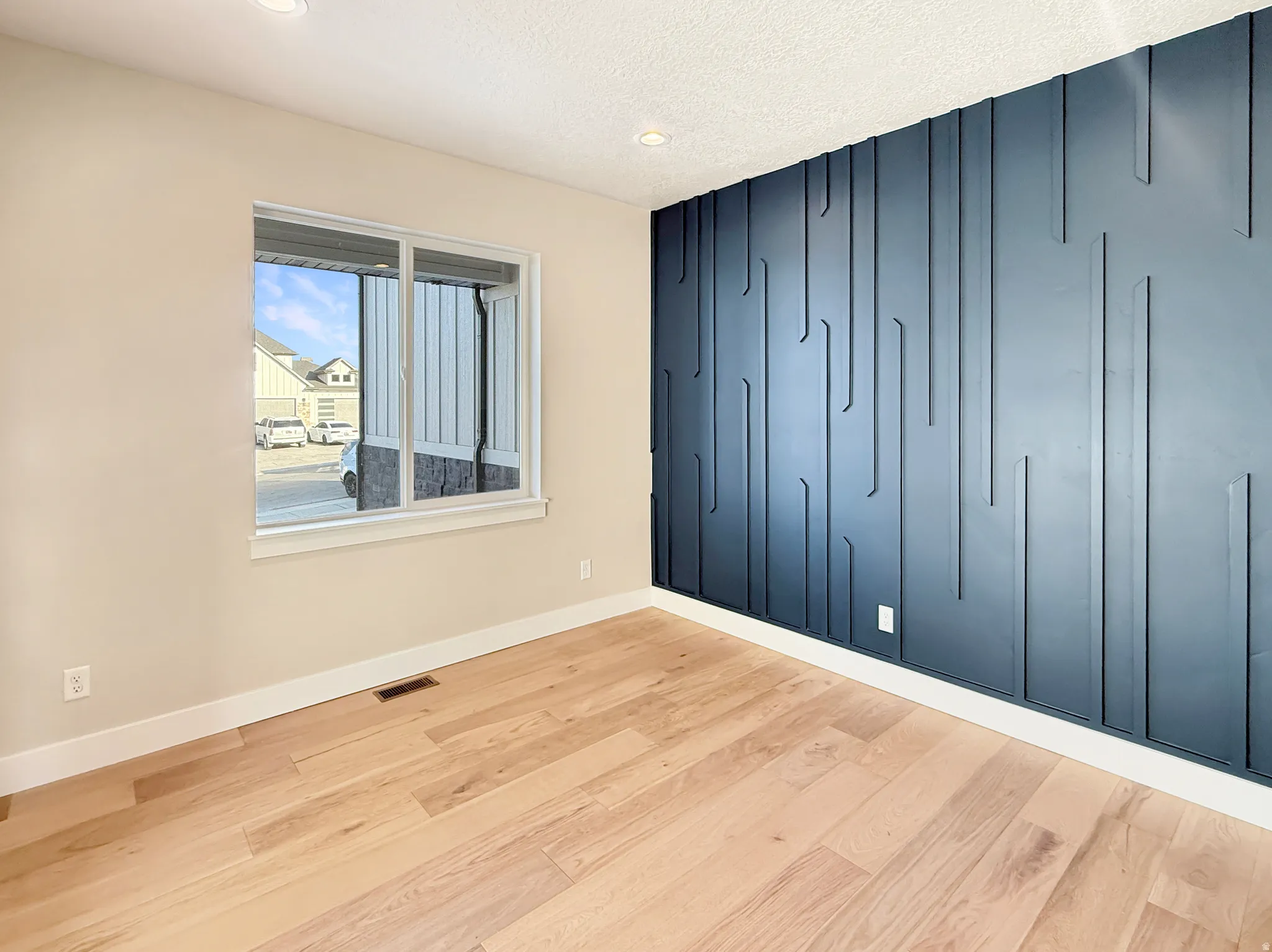 Feature wall with geometric paneling, recessed lighting, wood-finish flooring, white trim, and a window with white casing