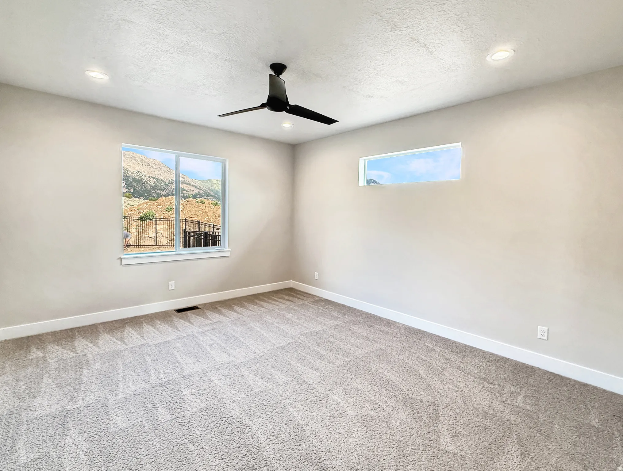 Spacious room featuring neutral carpeting, a contemporary black ceiling fan, and recessed lighting