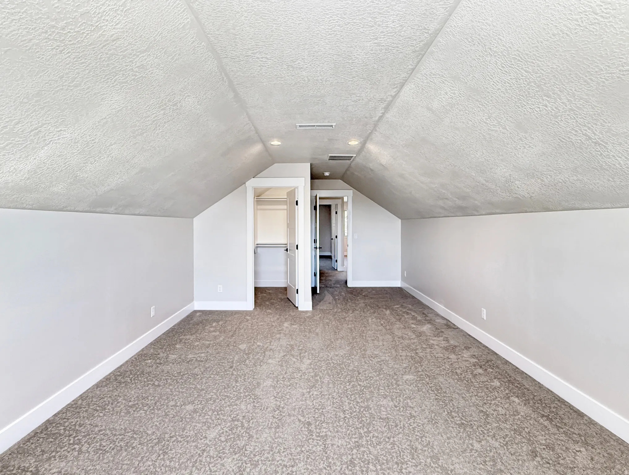 Spacious attic room featuring sloped ceilings, textured wall finishes, recessed lighting, and soft carpet flooring