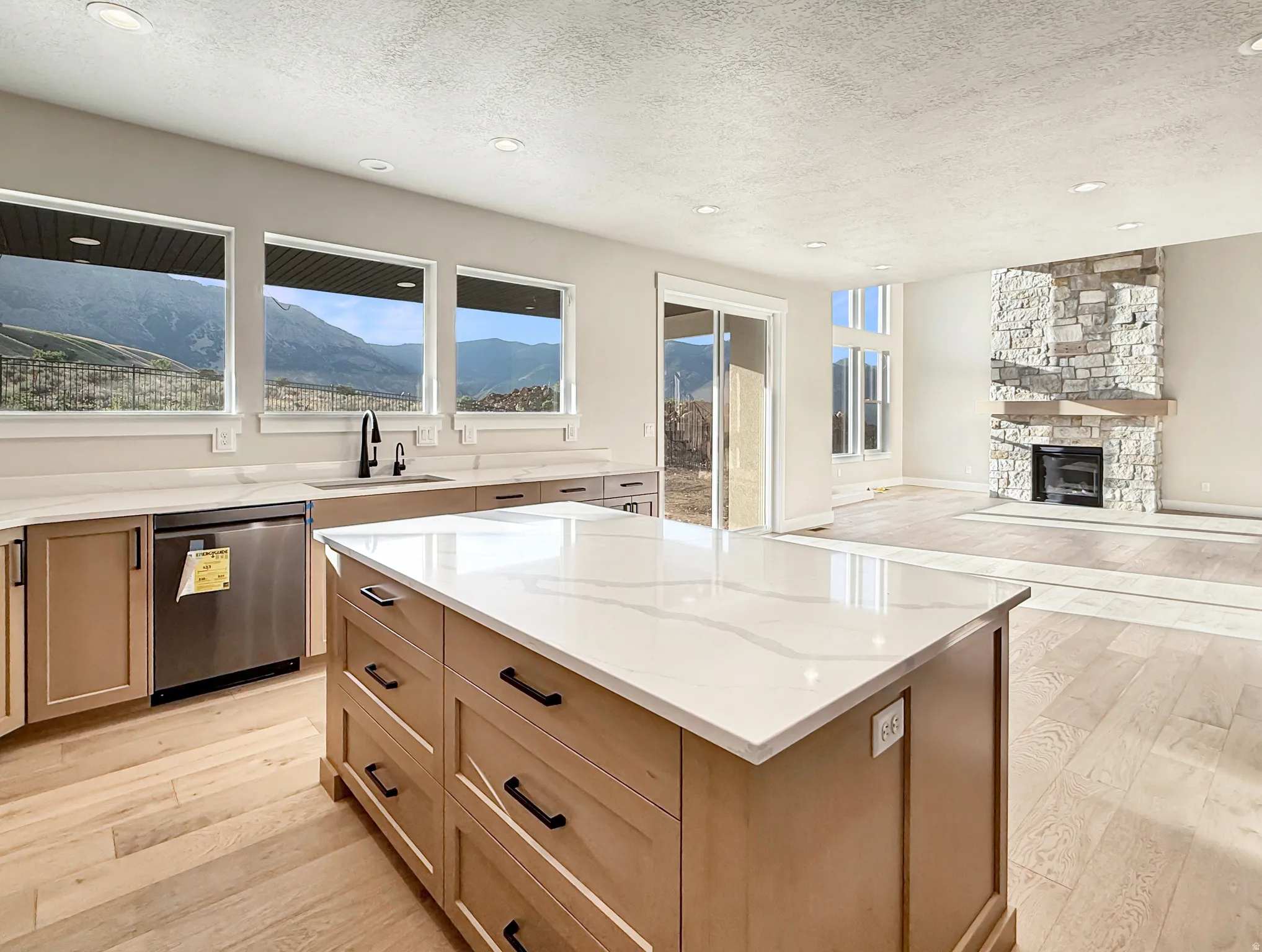 Modern kitchen featuring a large central island with a light-toned countertop, wood-finish cabinetry, and recessed lighting