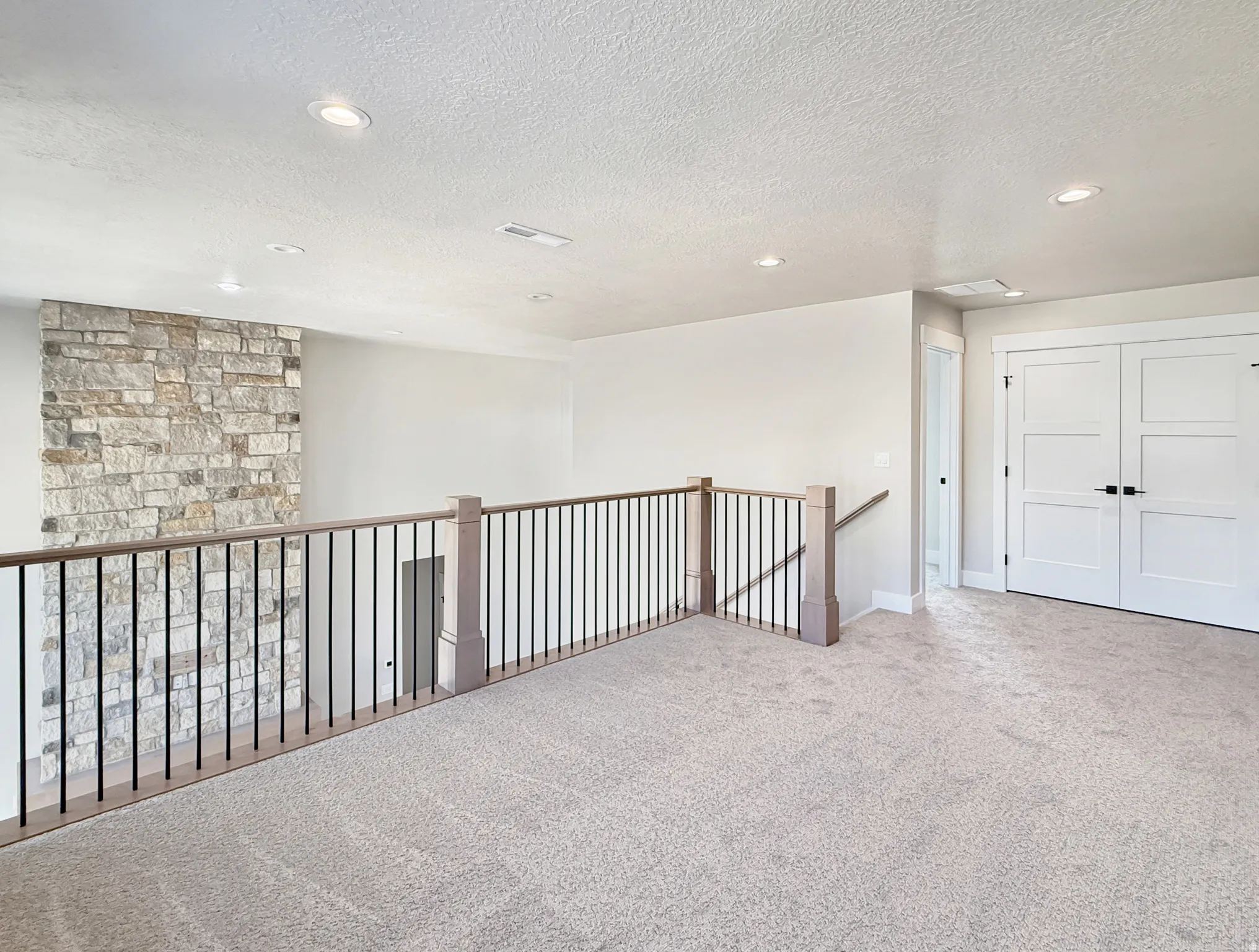 Expansive loft area featuring neutral carpeting, recessed ceiling lighting, and a stone accent wall