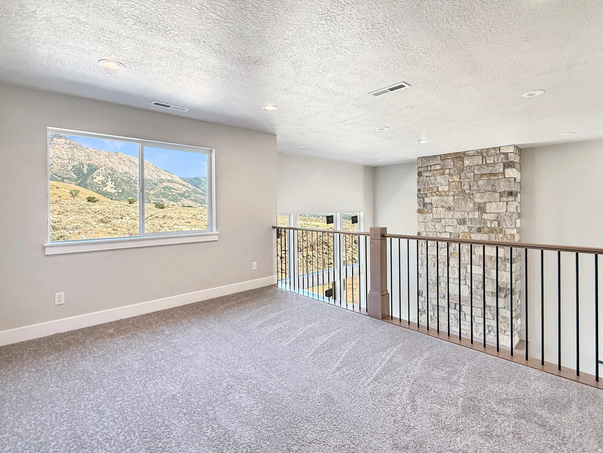 Carpeted loft area featuring a large window, recessed lighting, and a stacked stone accent wall