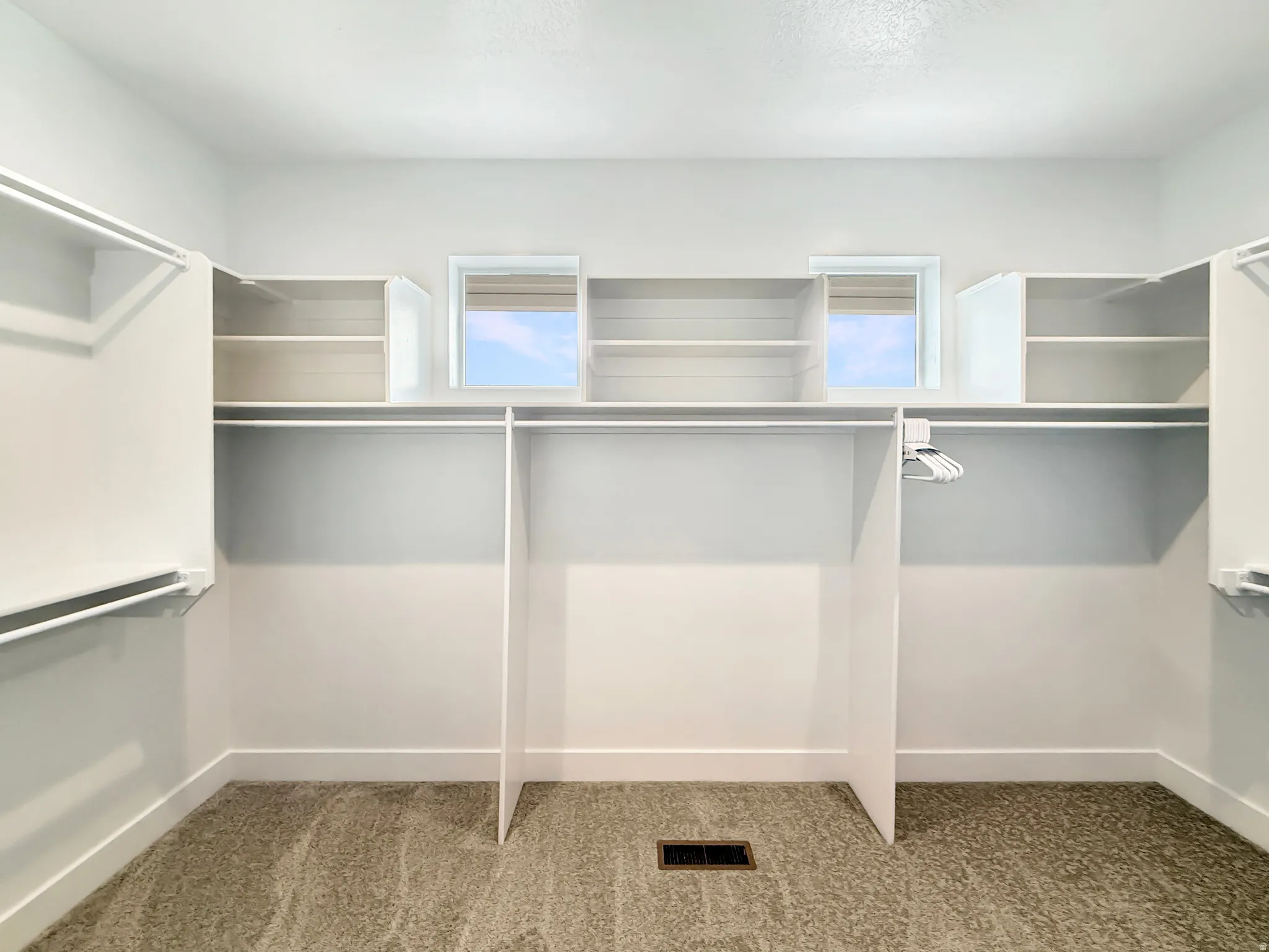 Spacious walk-in closet featuring white built-in shelving, multiple hanging rods, and light-colored carpeting