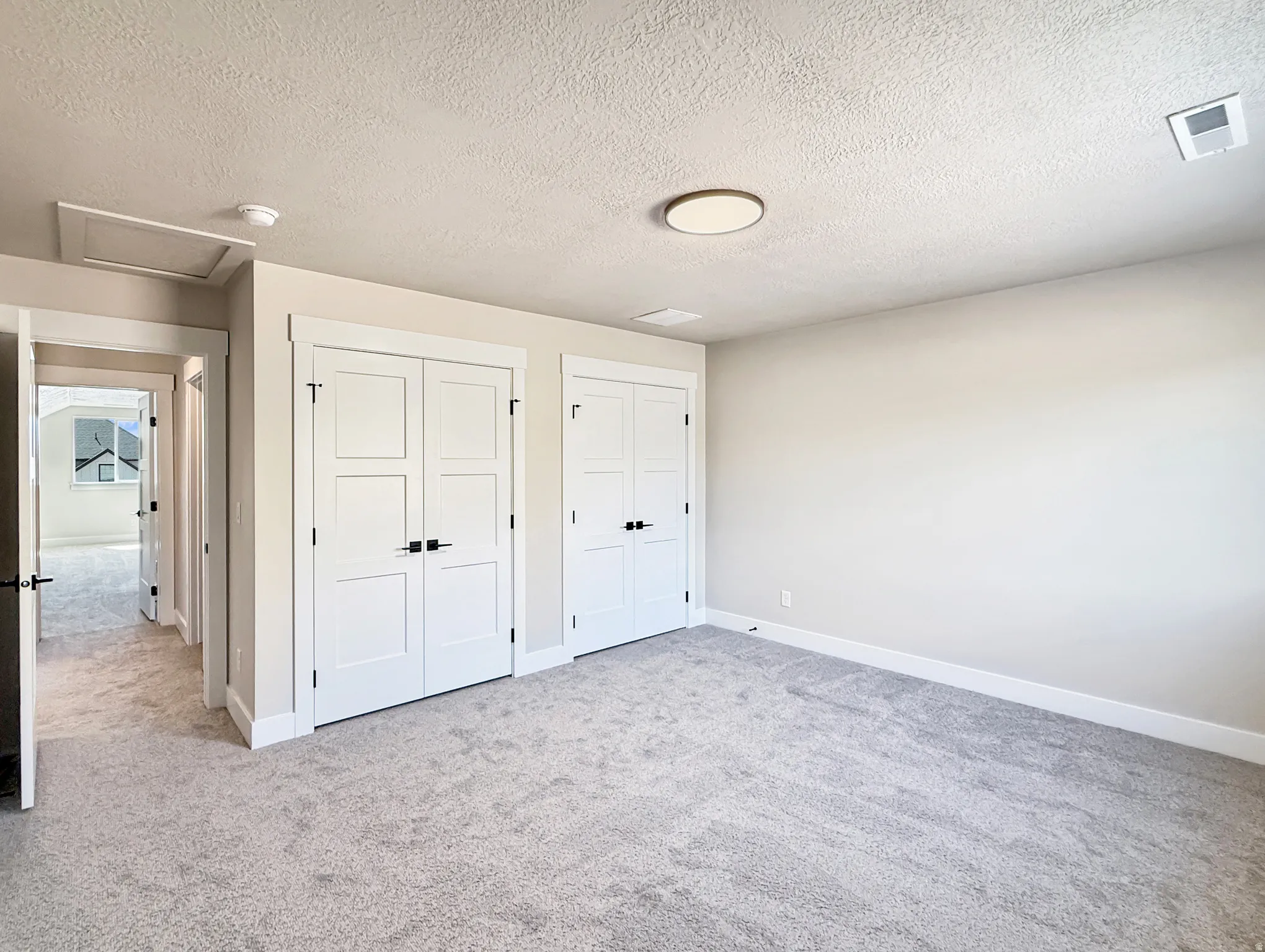 Spacious room featuring light gray carpeting, two sets of white bifold closet doors with dark hardware, and a modern circular flush-mount ceiling light