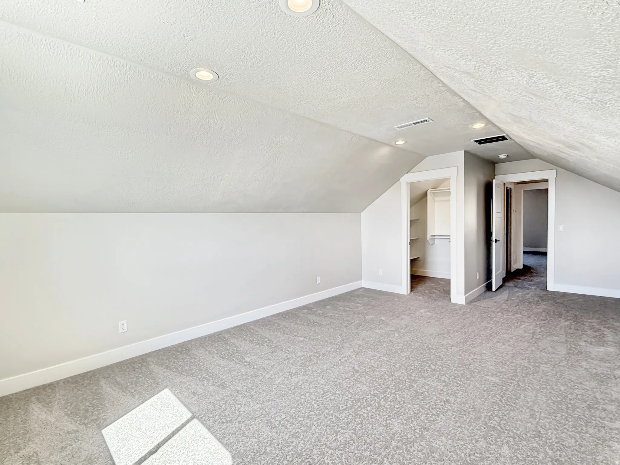 Spacious finished attic area featuring sloped ceilings, recessed lighting, neutral tone carpeting, and two integrated doorways