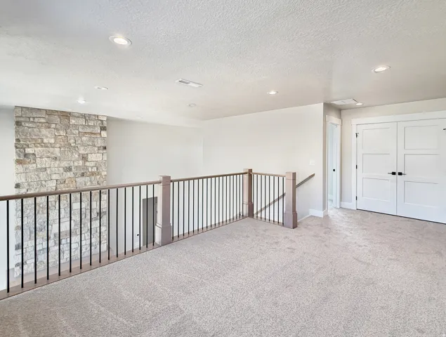Expansive loft area featuring neutral carpeting, recessed ceiling lighting, and a stone accent wall