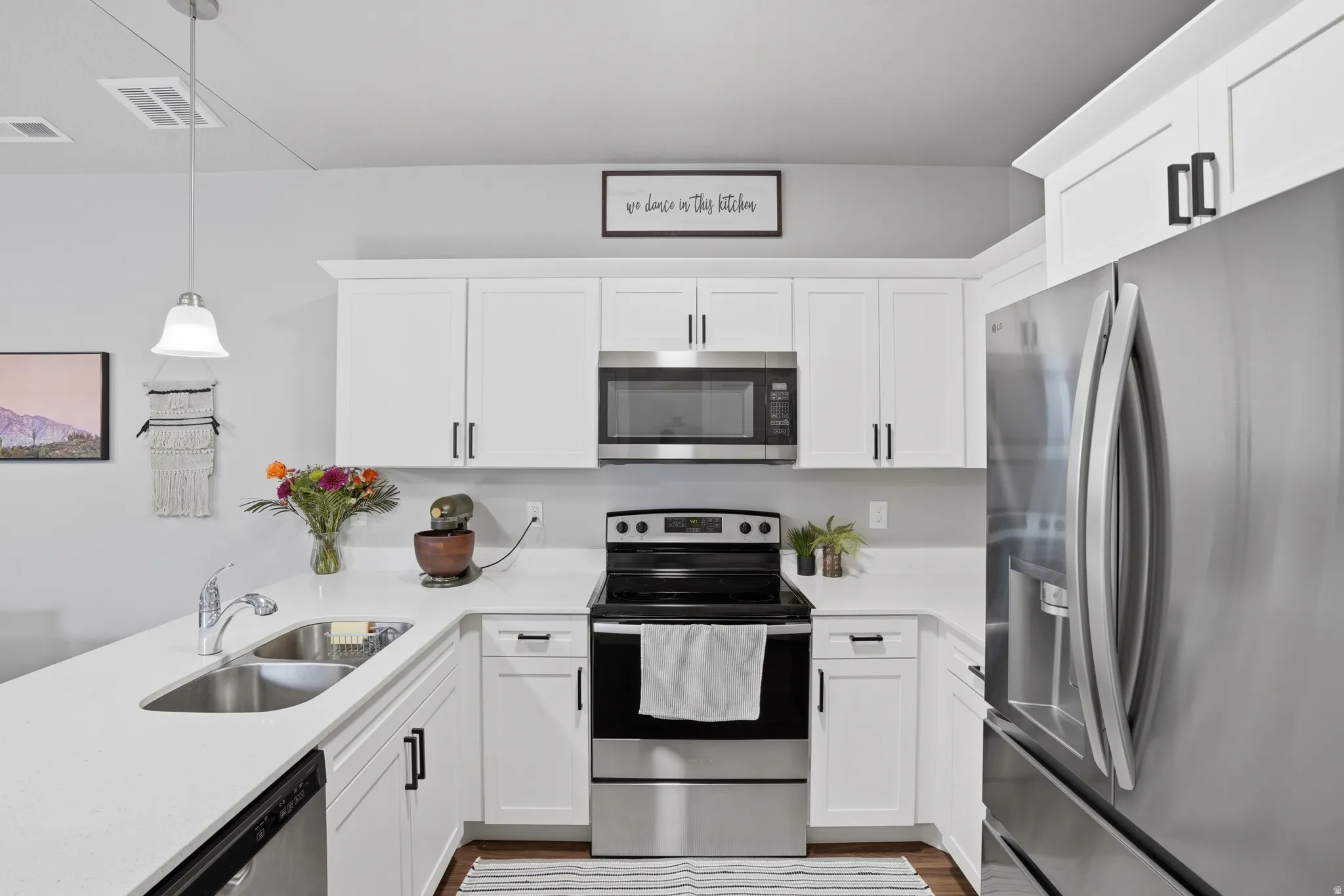 Modern kitchen featuring white cabinetry, stainless steel appliances, light countertops, and a stainless steel double-basin sink