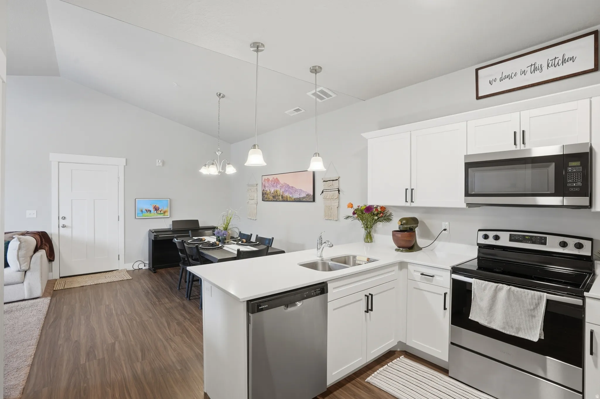 Open-concept kitchen and dining area featuring wood-finish flooring, white cabinetry with dark hardware, stainless steel appliances, and a vaulted ceiling