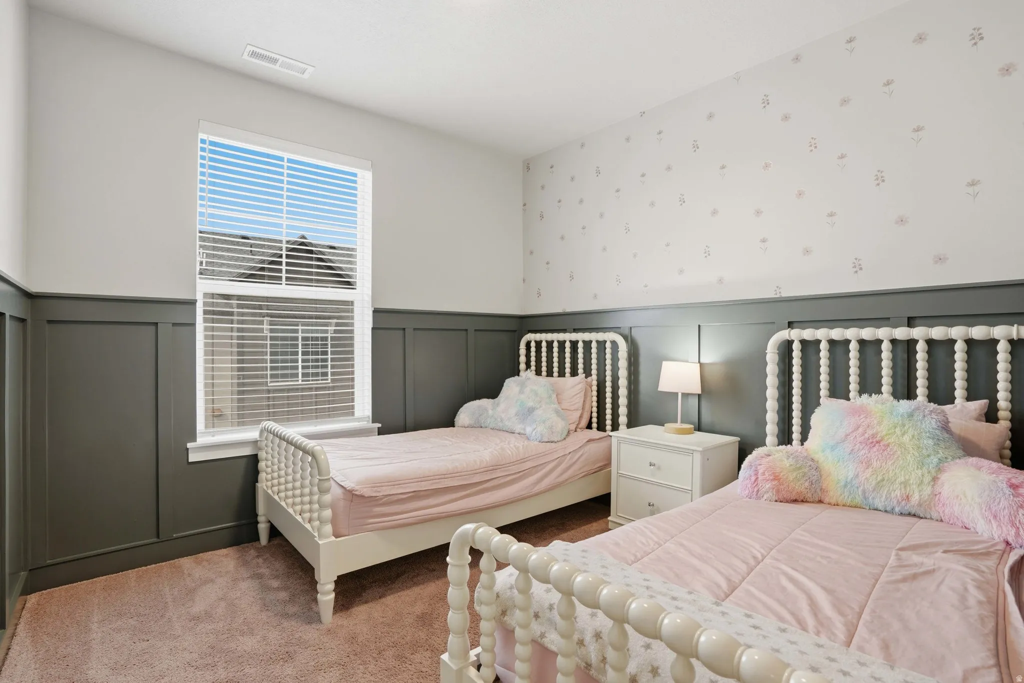 Bedroom featuring a single window with blinds, dark paneled wainscoting, light-toned wallpaper, and soft carpeting