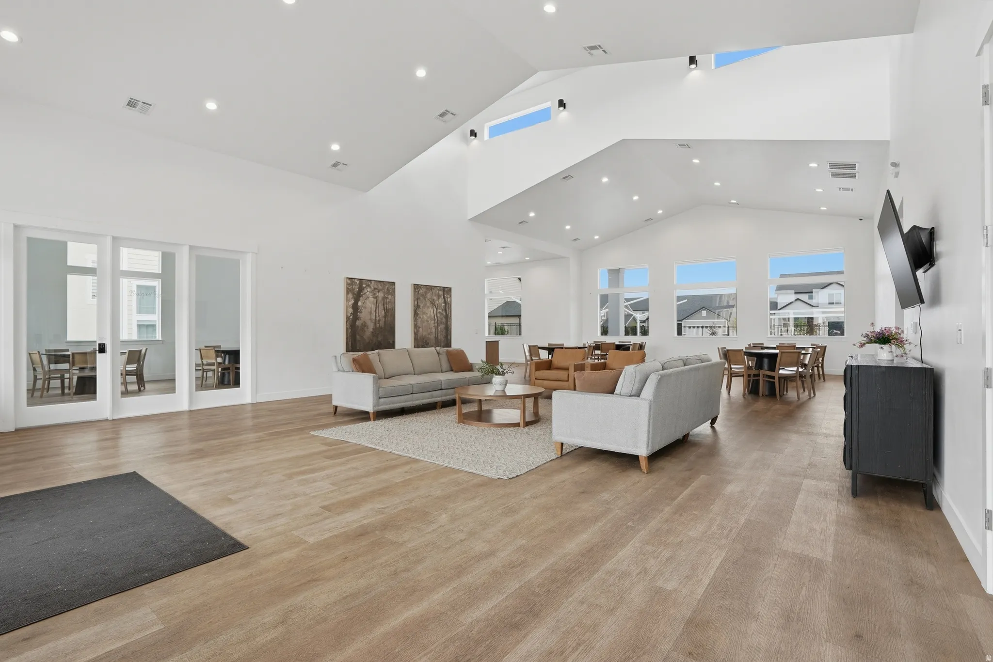 Spacious common area featuring vaulted ceilings with high windows, recessed lighting, and wood-finish flooring