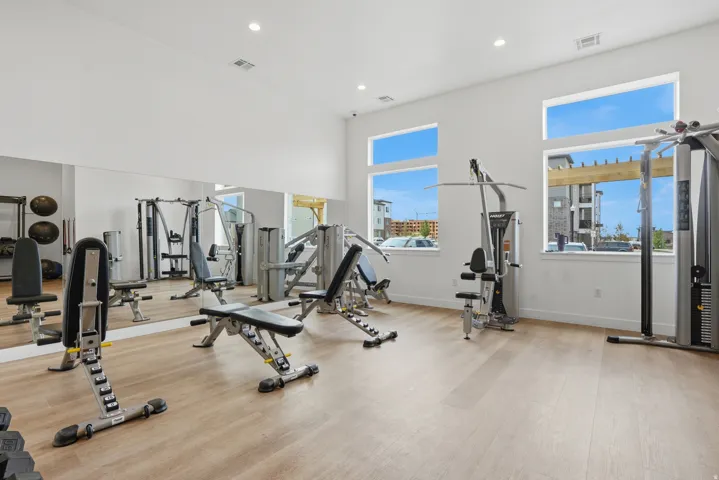 Fitness center featuring wood-finish flooring, ample natural light from multiple large windows, recessed lighting, and a mirrored wall