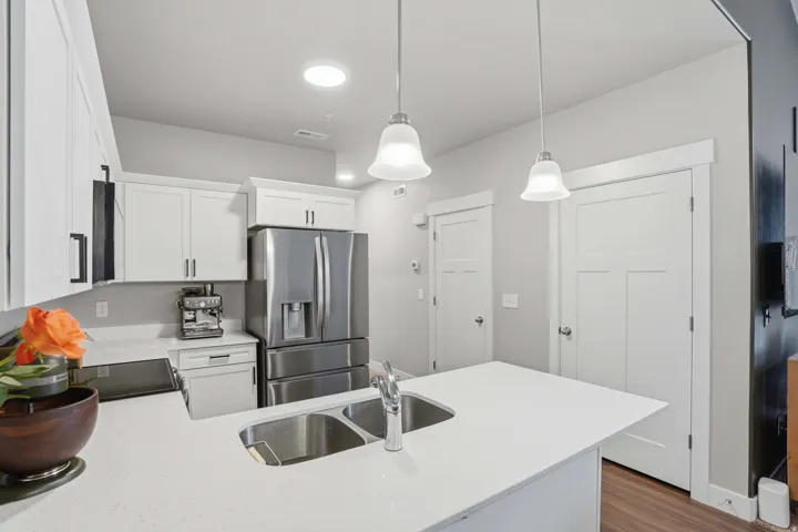 Contemporary kitchen featuring white cabinetry with black hardware, stainless steel French door refrigerator, quartz countertops, a dual basin undermount sink, and pendant lighting over the island