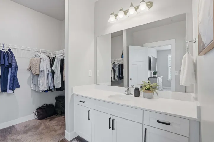 Vanity area with a single basin sink, white cabinetry with black hardware, and a large mirror