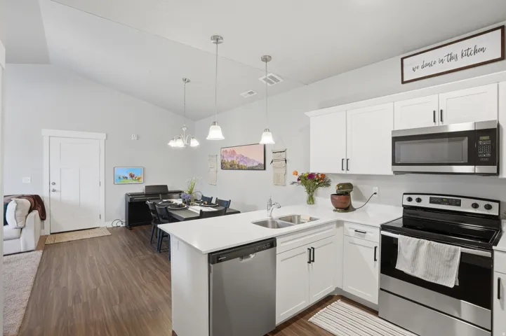 Open-concept kitchen and dining area featuring wood-finish flooring, white cabinetry with dark hardware, stainless steel appliances, and a vaulted ceiling