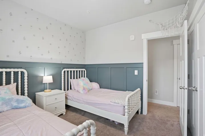 Bedroom featuring a paneled accent wall, neutral carpeting, white trim, and a white interior door