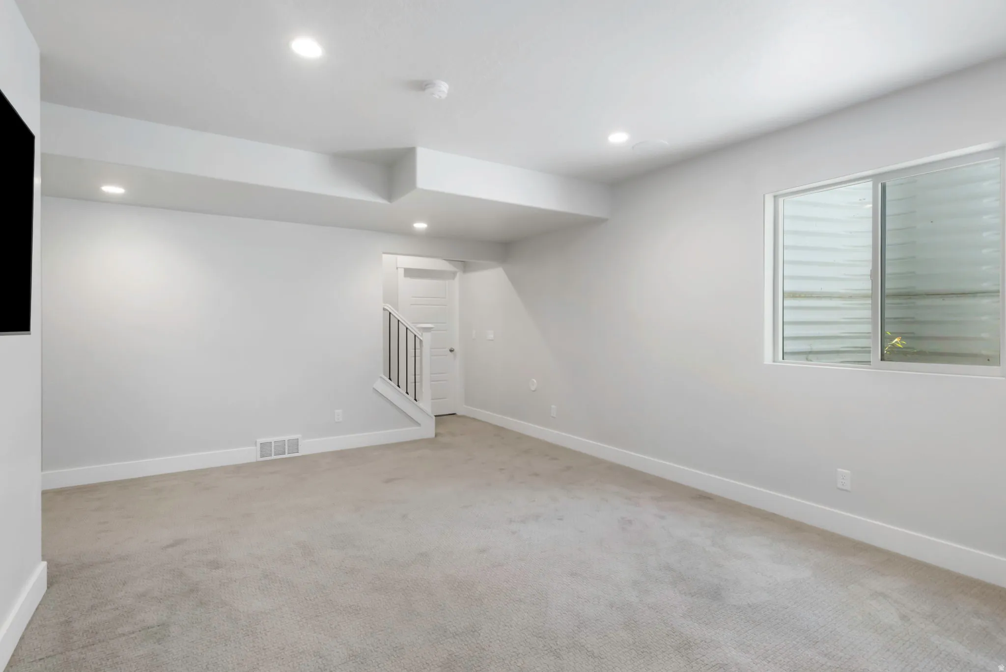 Spacious carpeted room featuring recessed lighting, a neutral color palette, white baseboards, and a window with horizontal blinds