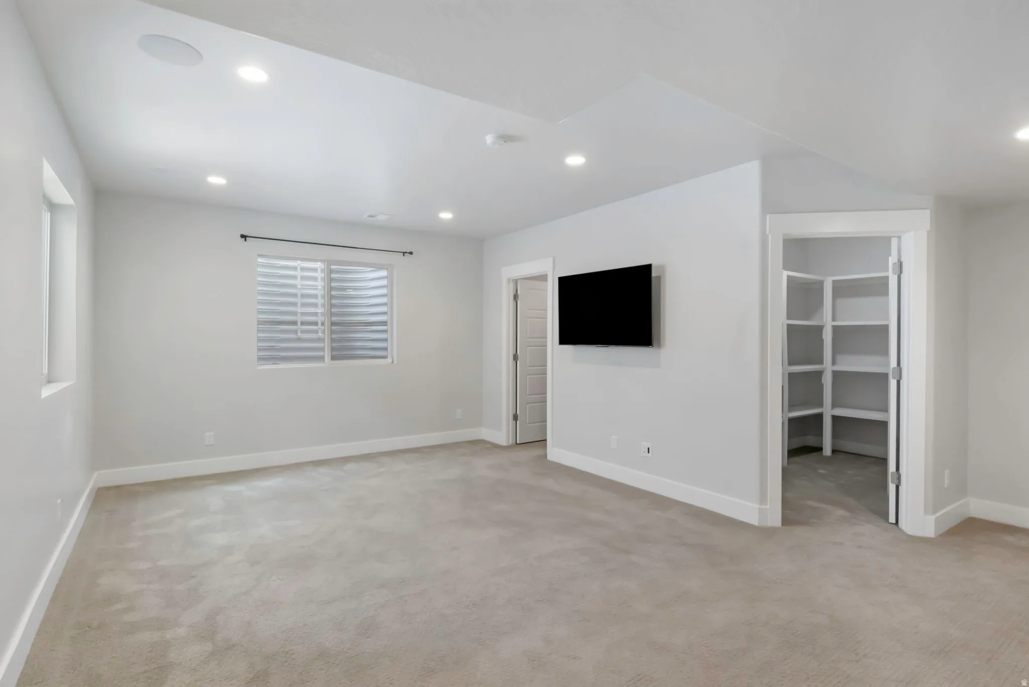 Spacious room featuring neutral carpeting, recessed lighting, and a wall-mounted display