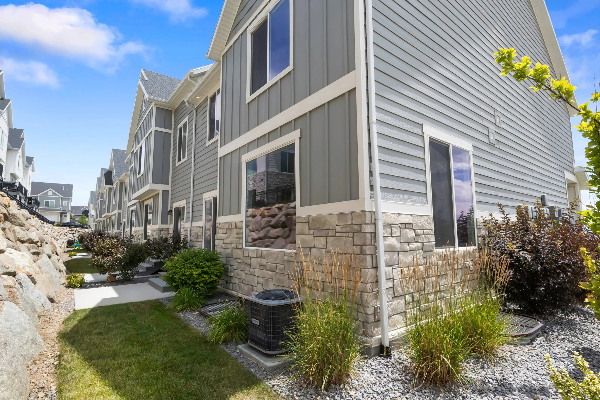 Exterior featuring grey siding, stone veneer accents, multiple windows, and a paved walkway