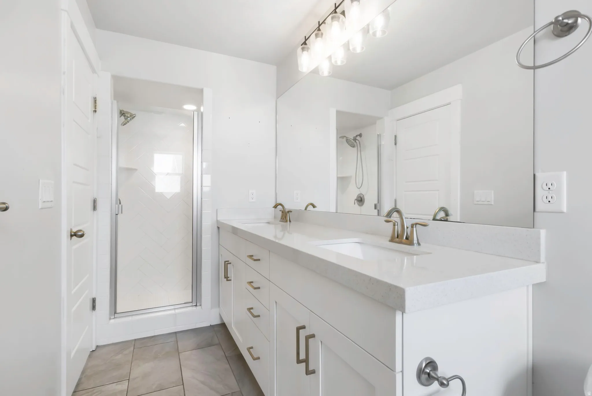 Spacious bathroom featuring a dual vanity with white cabinetry, light-toned countertops, and brushed gold-tone fixtures