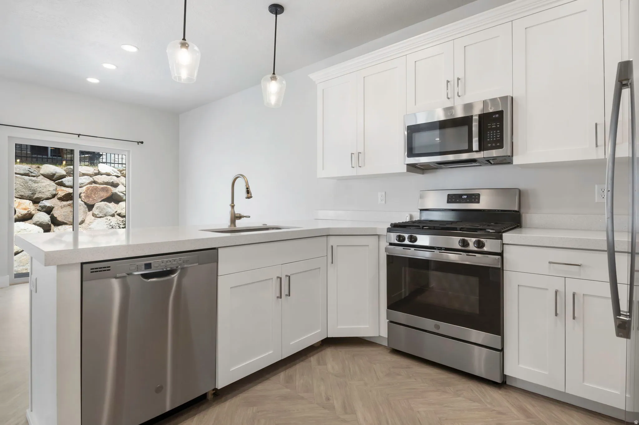 Modern kitchen featuring white shaker cabinetry, stainless steel appliances, light countertops, and wood-finish herringbone flooring